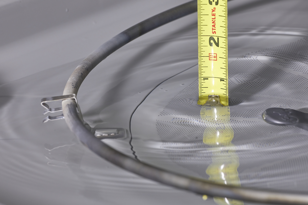 A tape measure measuring pooled water in the bottom of a dishwasher.