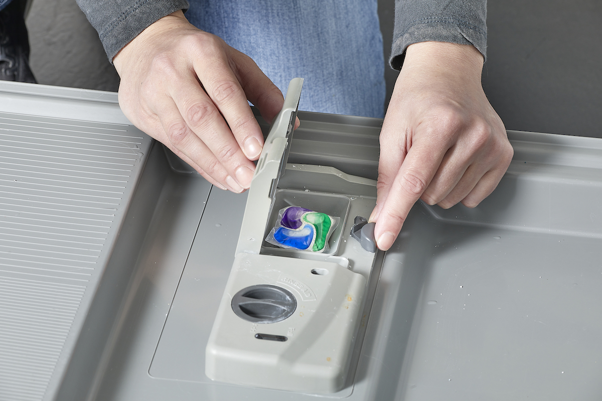 Person handling a dishwasher pod dispenser with a pod inside.