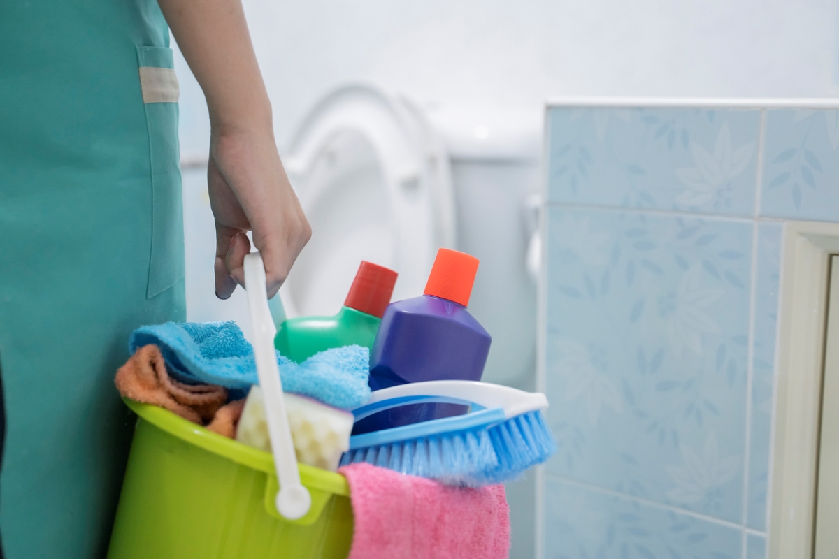 Woman holding caddy with cleaning supplies.