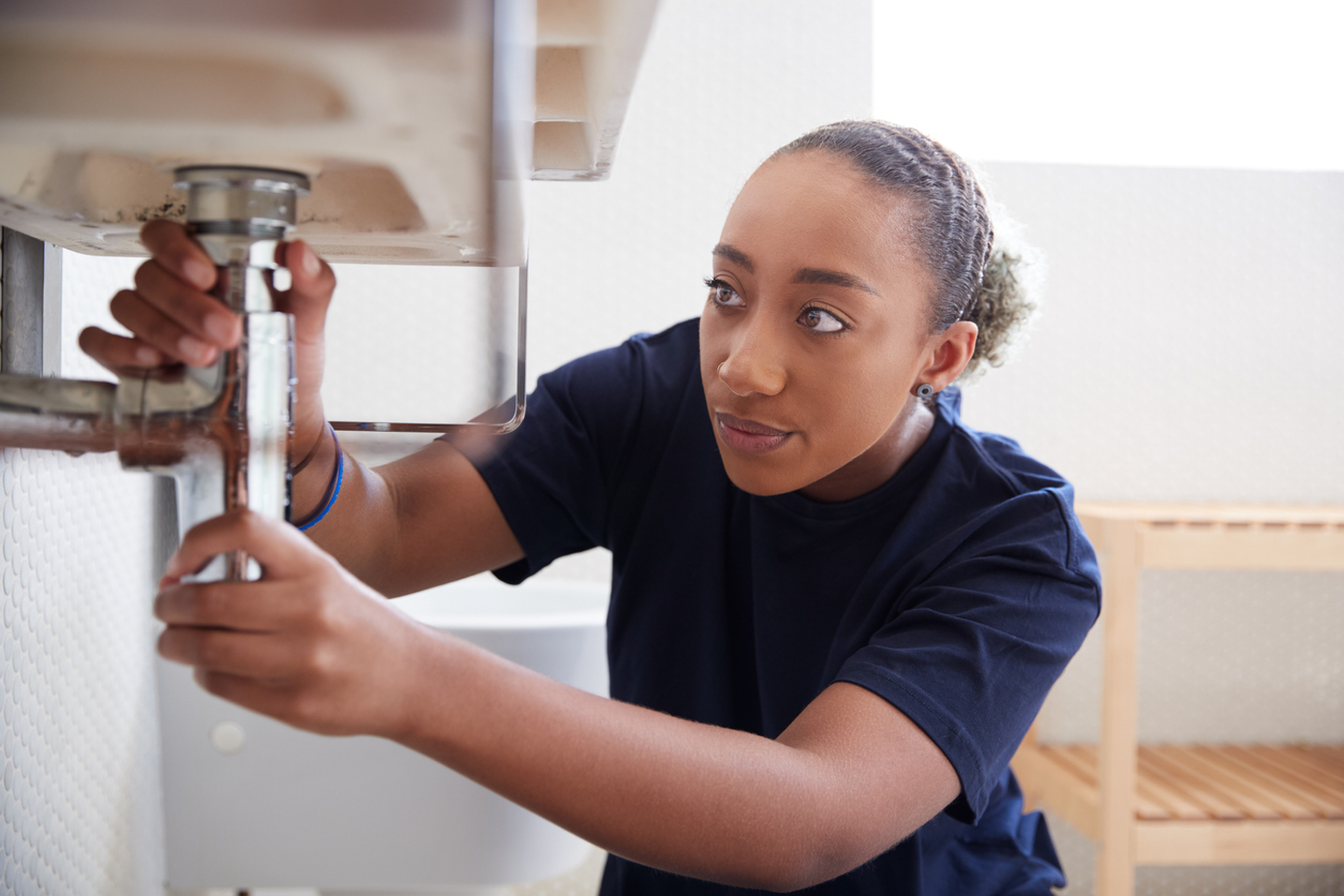 A-young-woman-inspects-the-plumbing-underneath-a-sink.