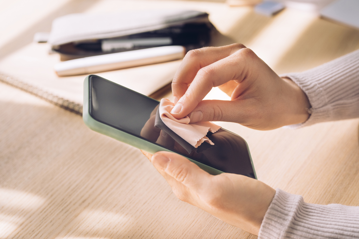 Close up shot of an unrecognizable woman cleaning the surface of her smartphone at her home office.