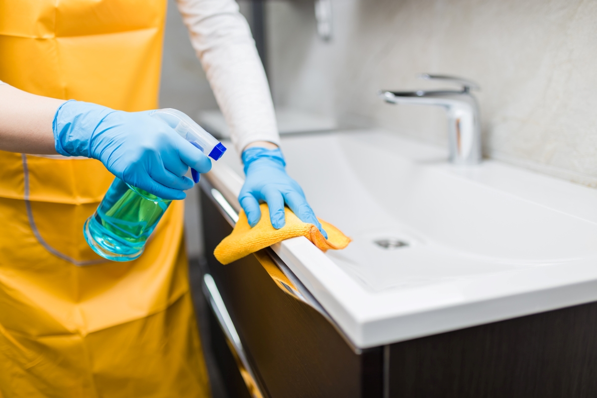 Person with gloves spraying bathroom sink.