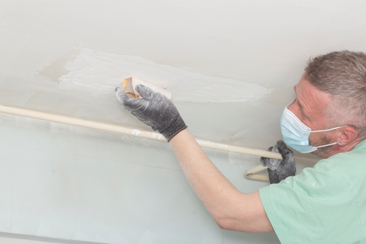 Man with mask sanding ceiling patch