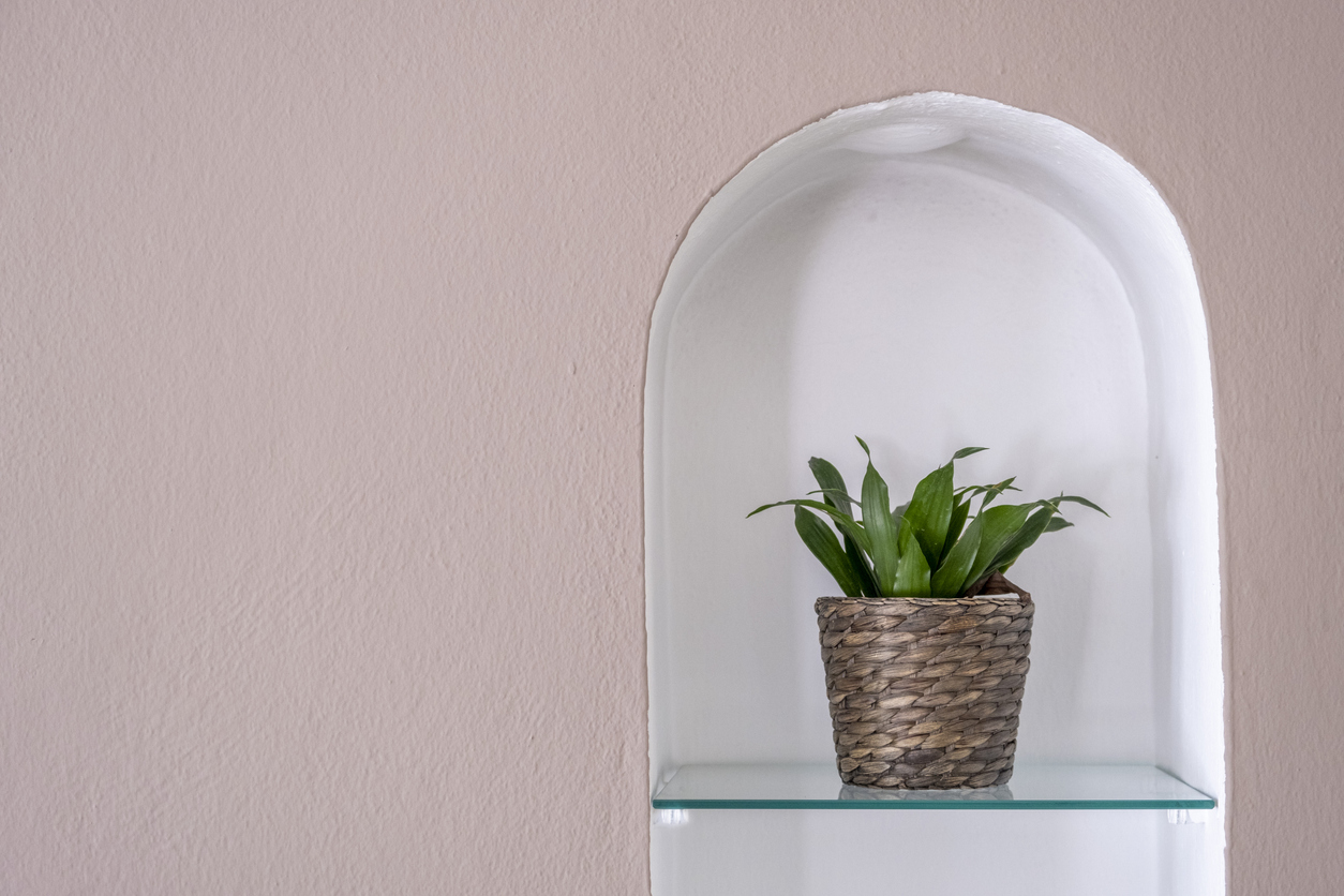 Rattan flower pot with green leaves in a wall niche on pink wall