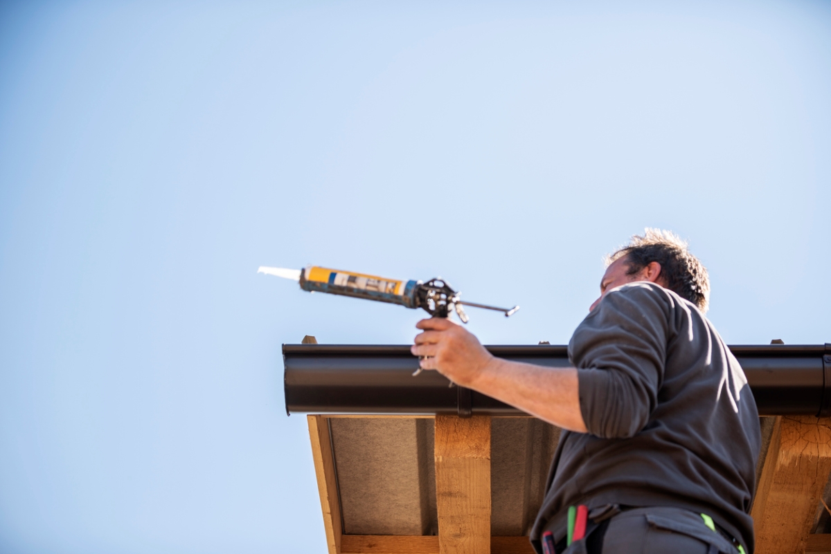 person holding sealant gun near roof