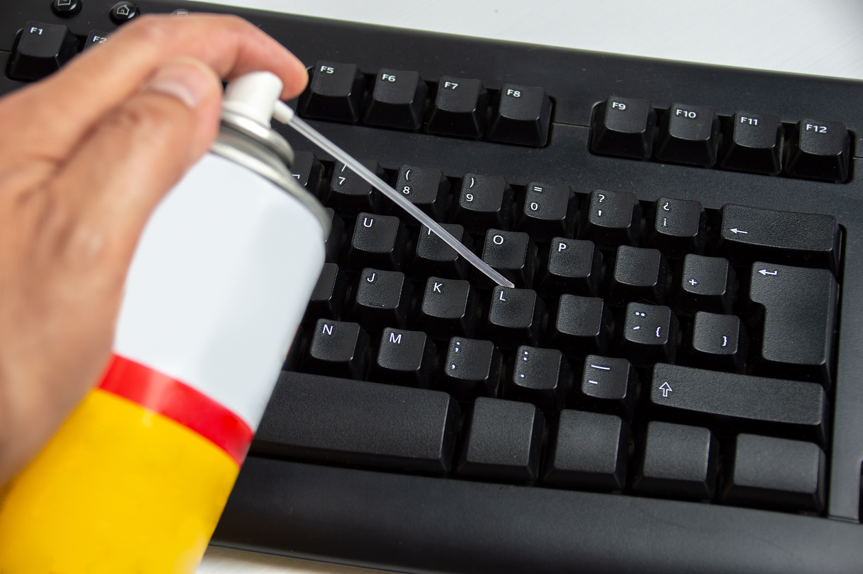 Close up of man cleaning dust from computer keyboard with air pressure cleaner