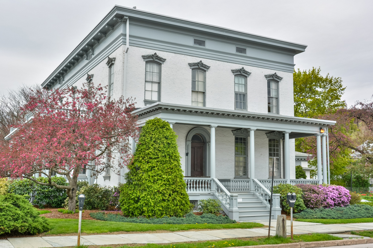 A-historic-pale-grey-home-is-surrounded-by-green-and-pink-landscape-design.