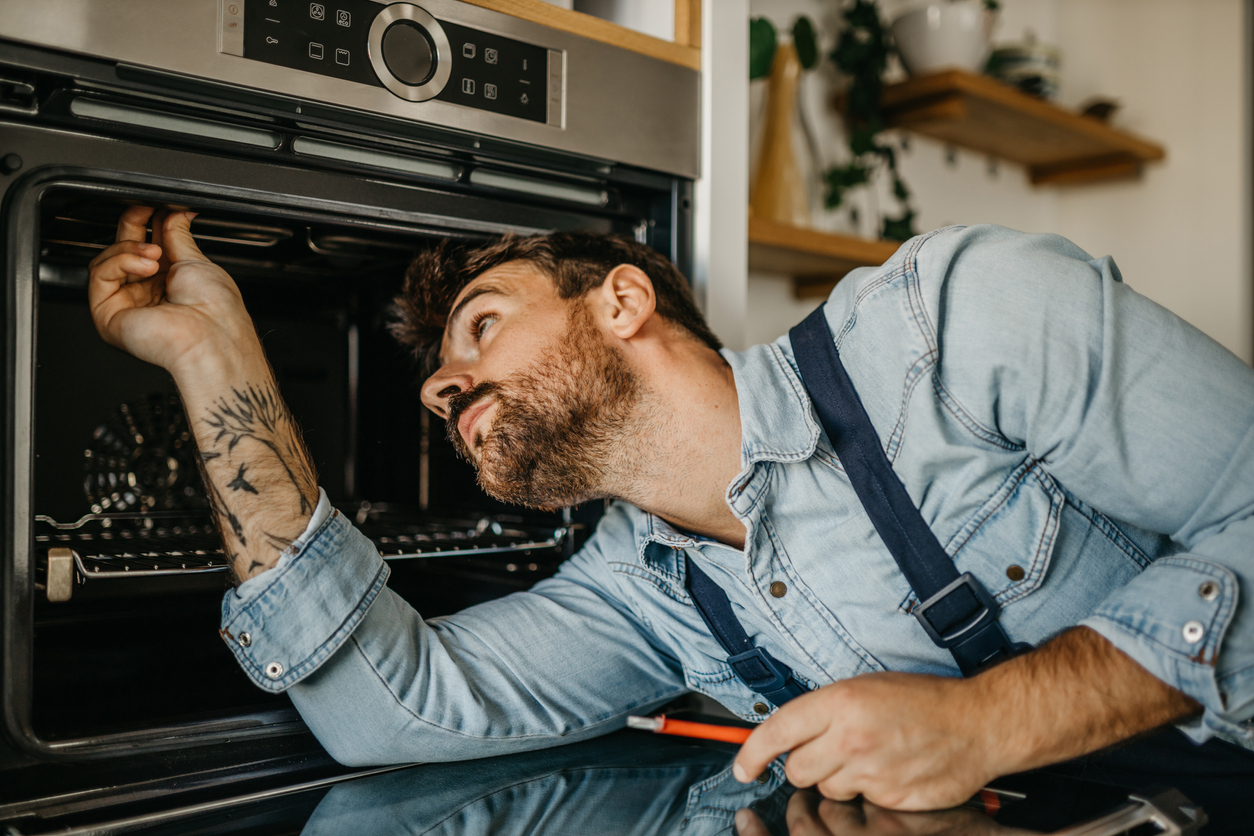 Worker checking and repairing an oven in the kitchen.