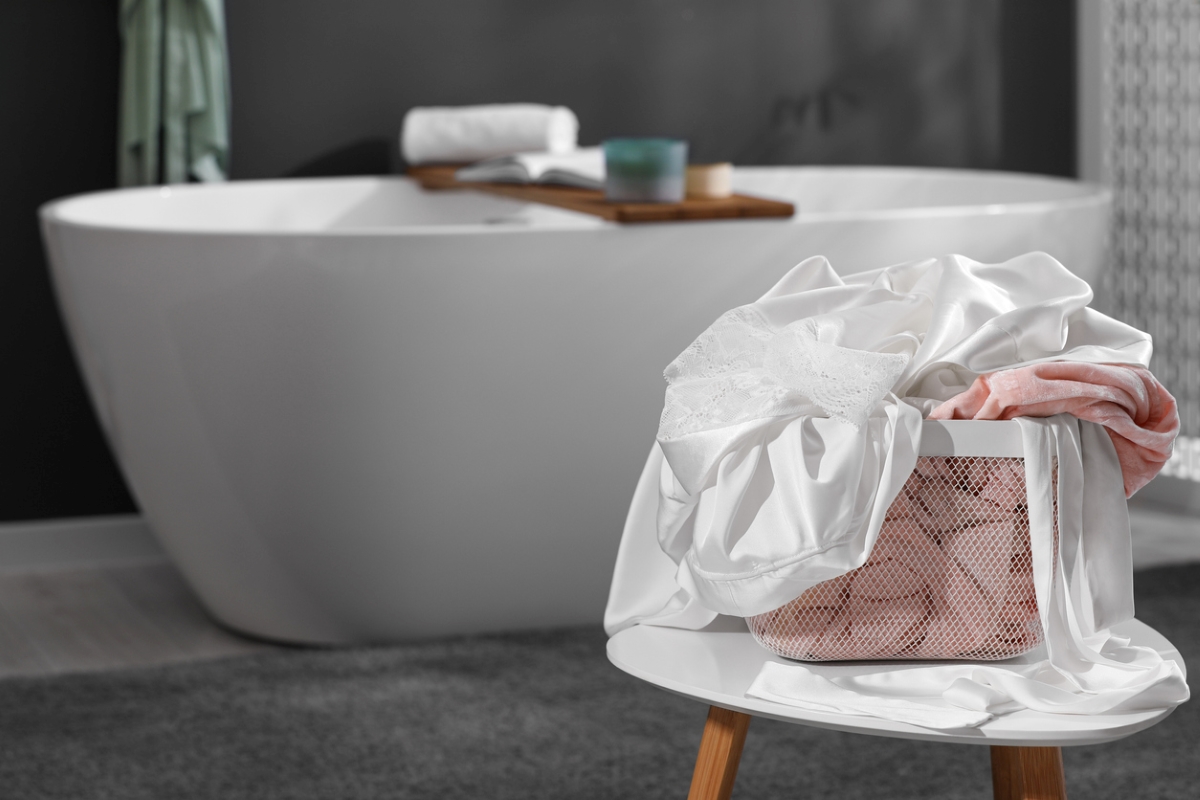 Laundry basket filled with clothes next to tub.