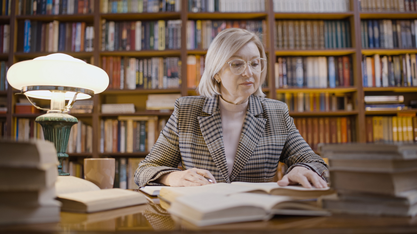 Senior woman librarian working late, reading through new books, occupation, scientific research