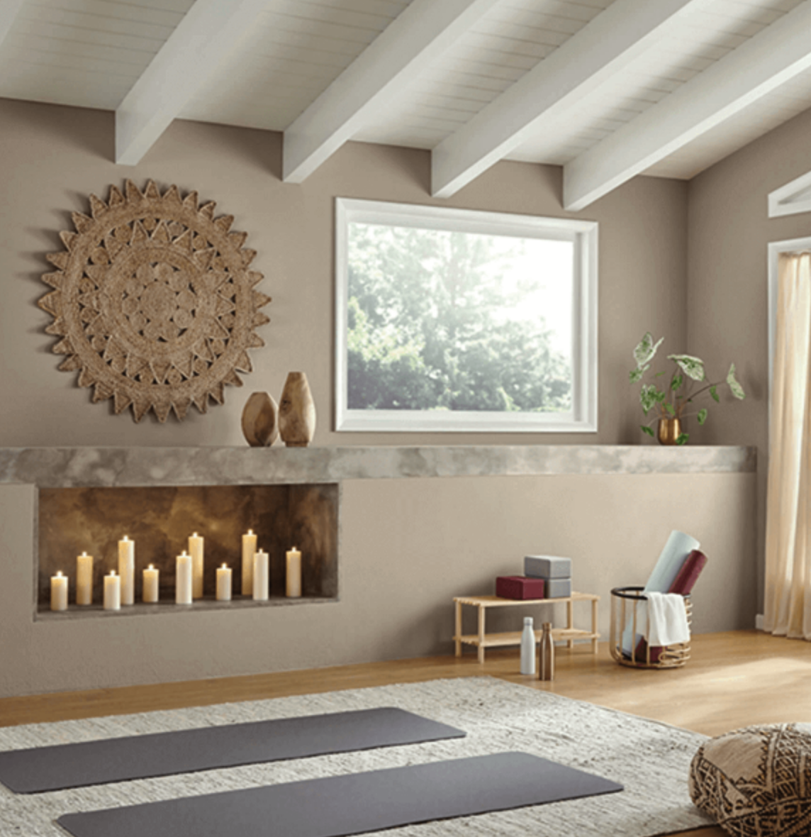 A home yoga studio with candles in an inset shelf and an angled ceiling with warm grey walls and yoga mats set up on the floor