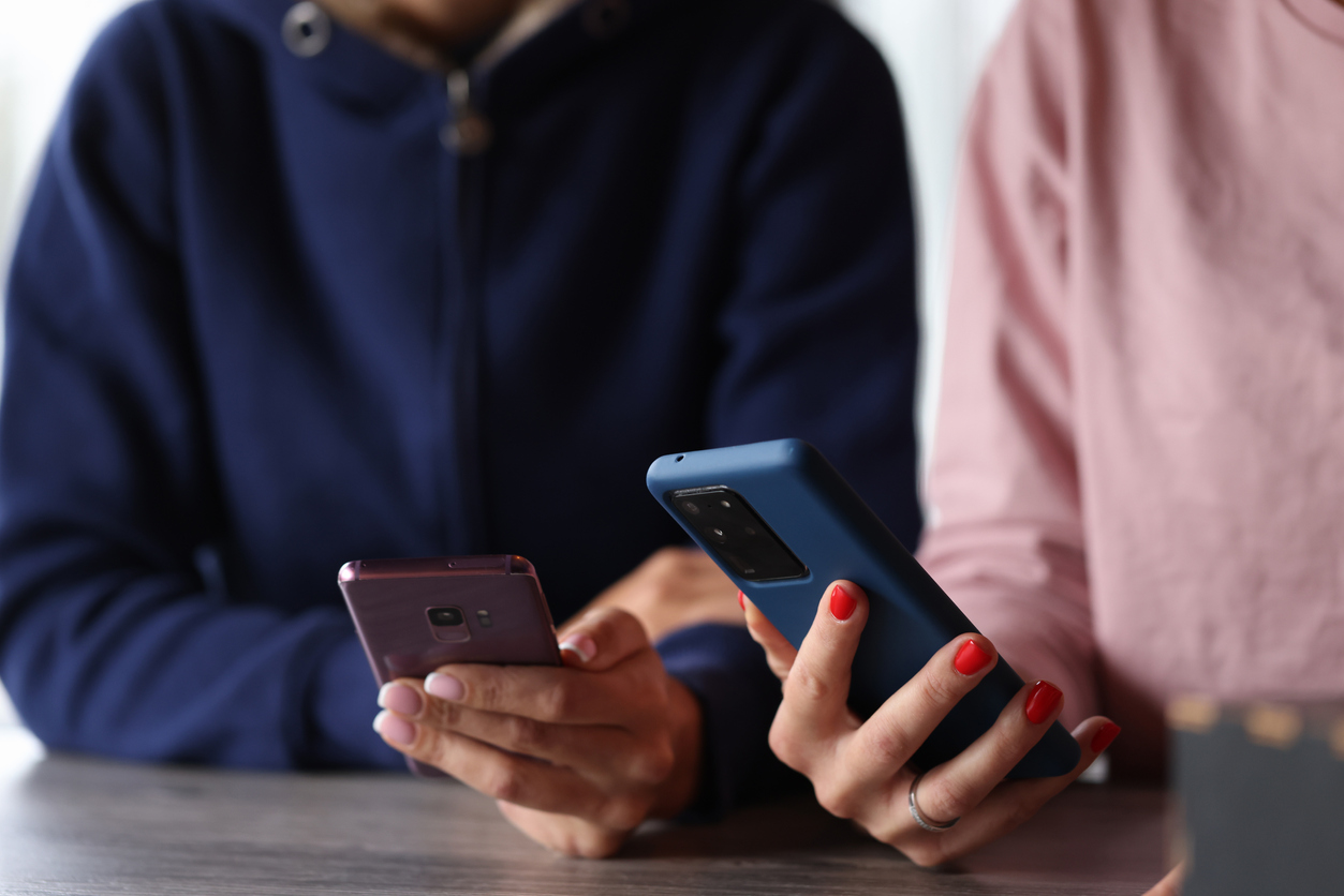 Two women holding different brands of smartphones near one another.