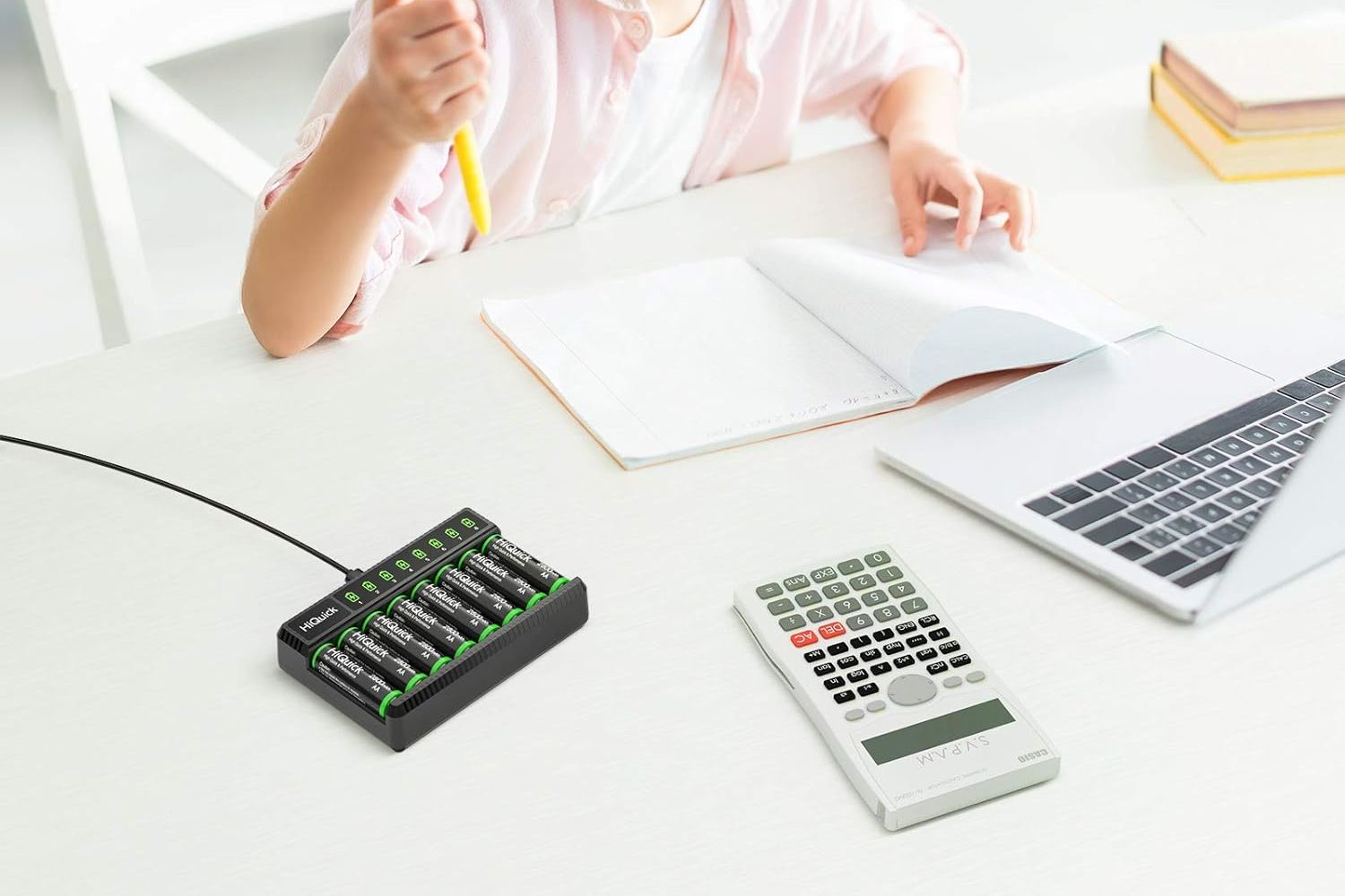 A child doing homework at a white desk with the best rechargeable batter charger , a calculator, and a laptop.