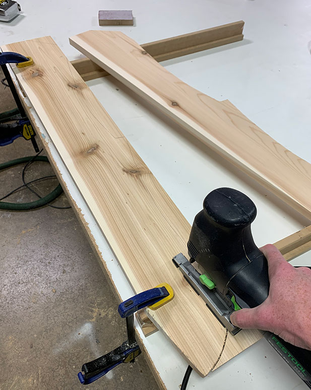 A woodworker cutting a piece of cedar in a workshop for building a DIY Adirondack chair.