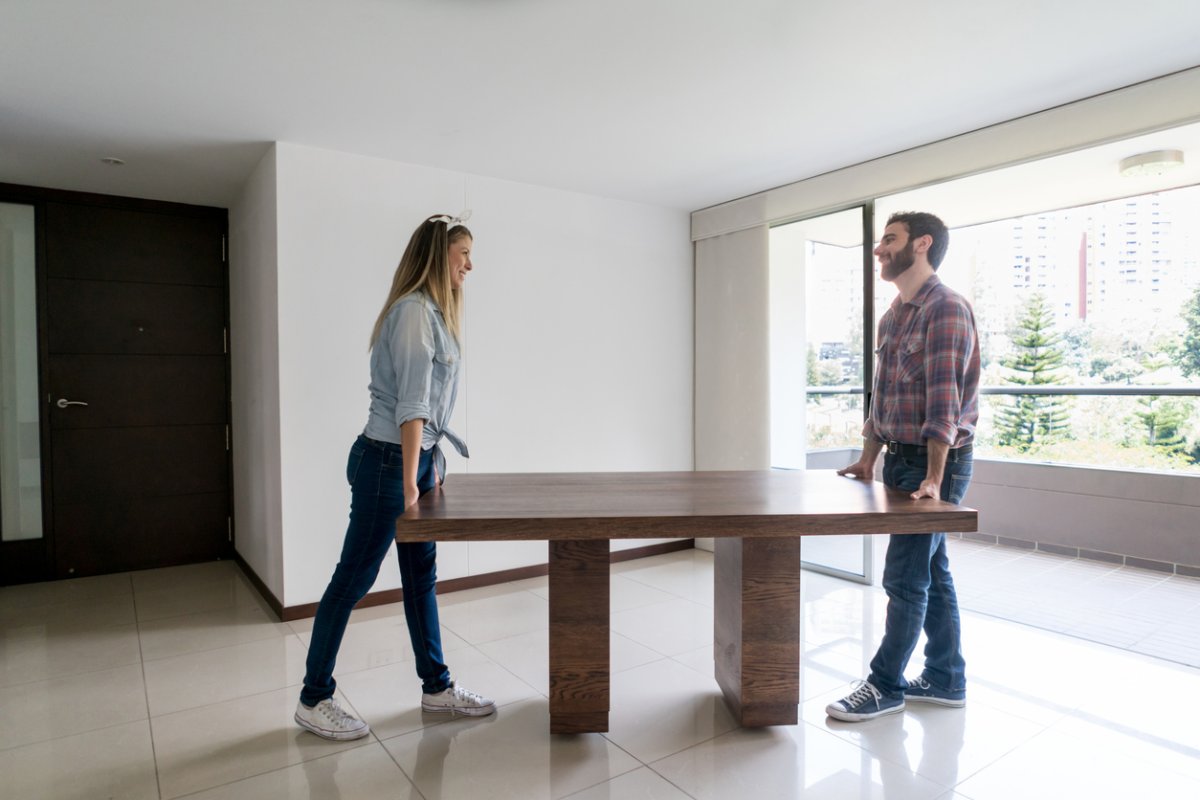 Young couple moving into their new place carrying a dining table while talking and having fun looking very happy