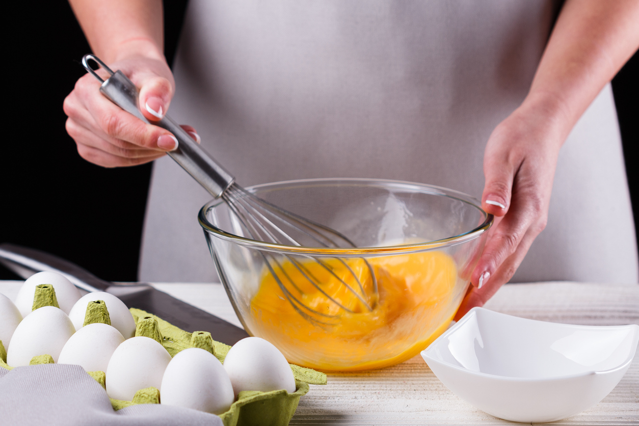 young woman in a gray aprons breaks the eggs.