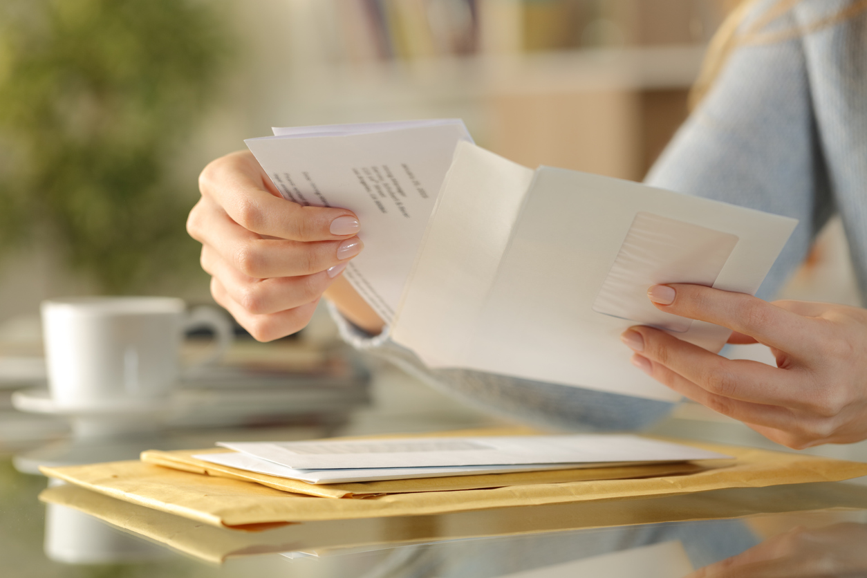 Close up of a woman's hands opening bills in the mail while sitting at her desk.