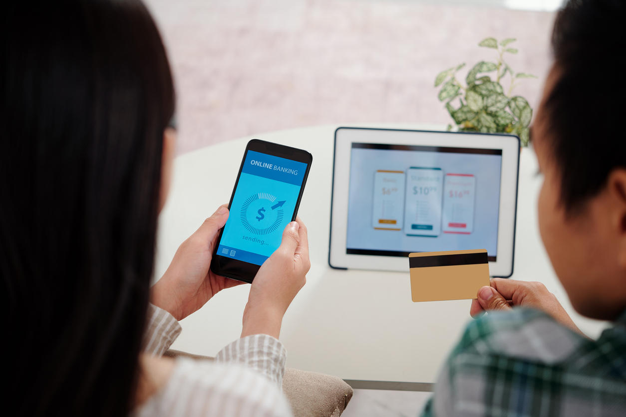 Couple choosing online plan on screen of digital tablet and paying via mobile banking app, view from the back