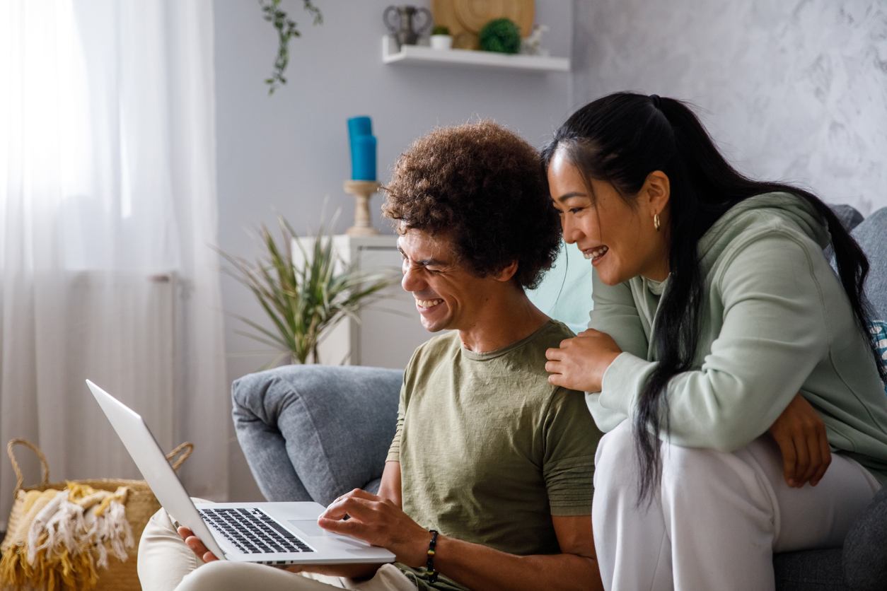 Cheerful couple looking at something on laptop in their living room.