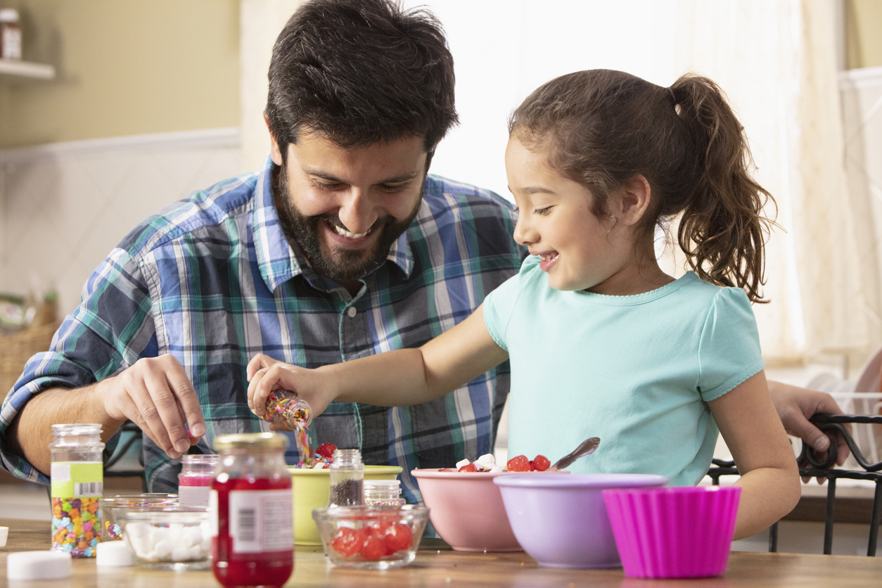 Father and daughter putting sprinkles on ice cream sundaes together.