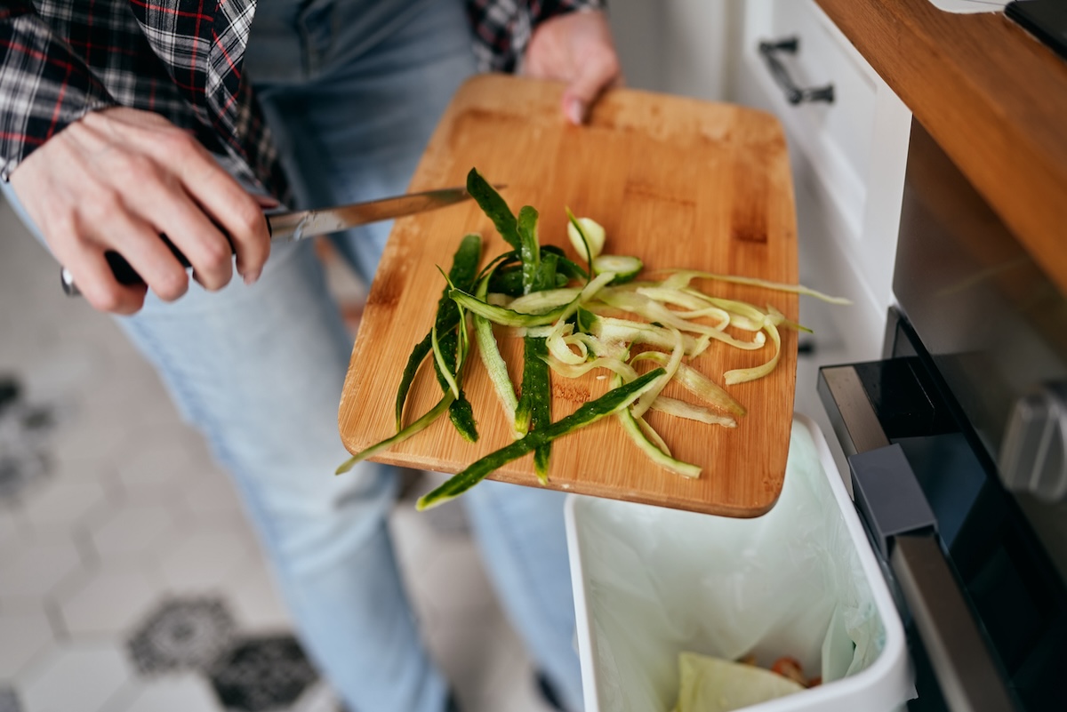 Woman scraping vegetable scraps into an organics recycling and composting bin in a kitchen.