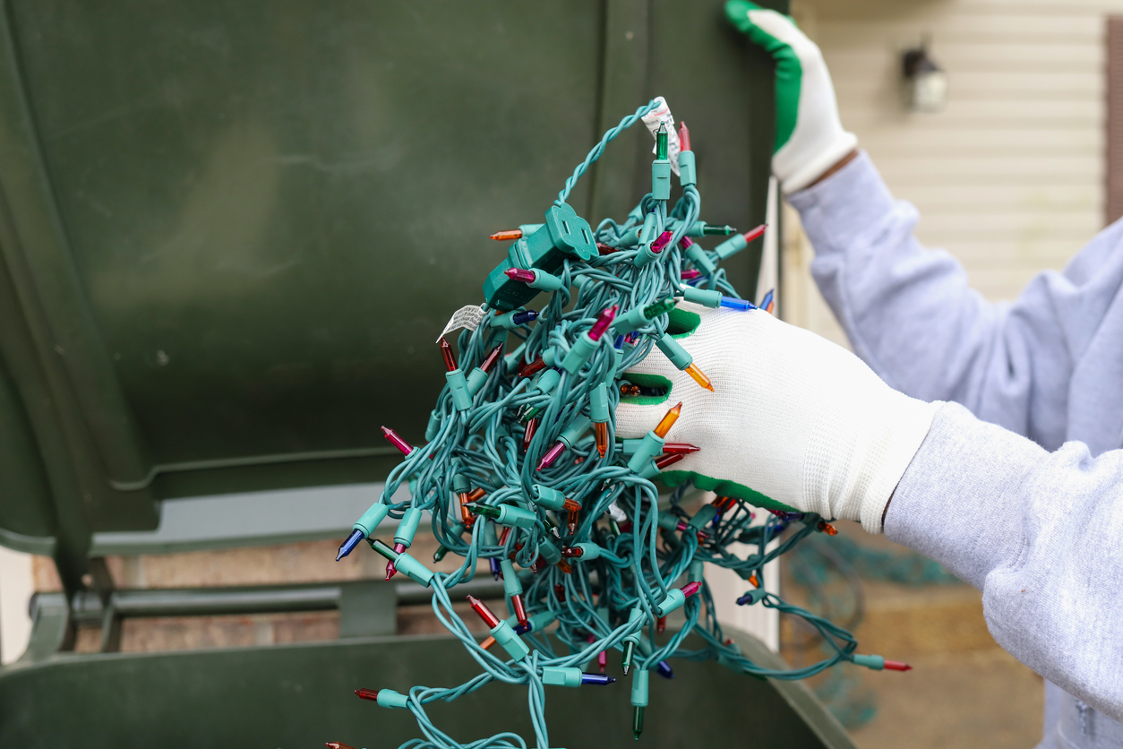 Throwing away damaged Christmas lights in a garage bin.