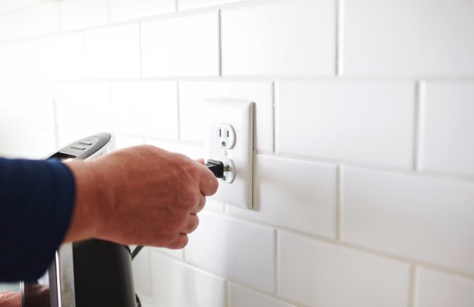 A person unplugging a coffee maker in a kitchen.