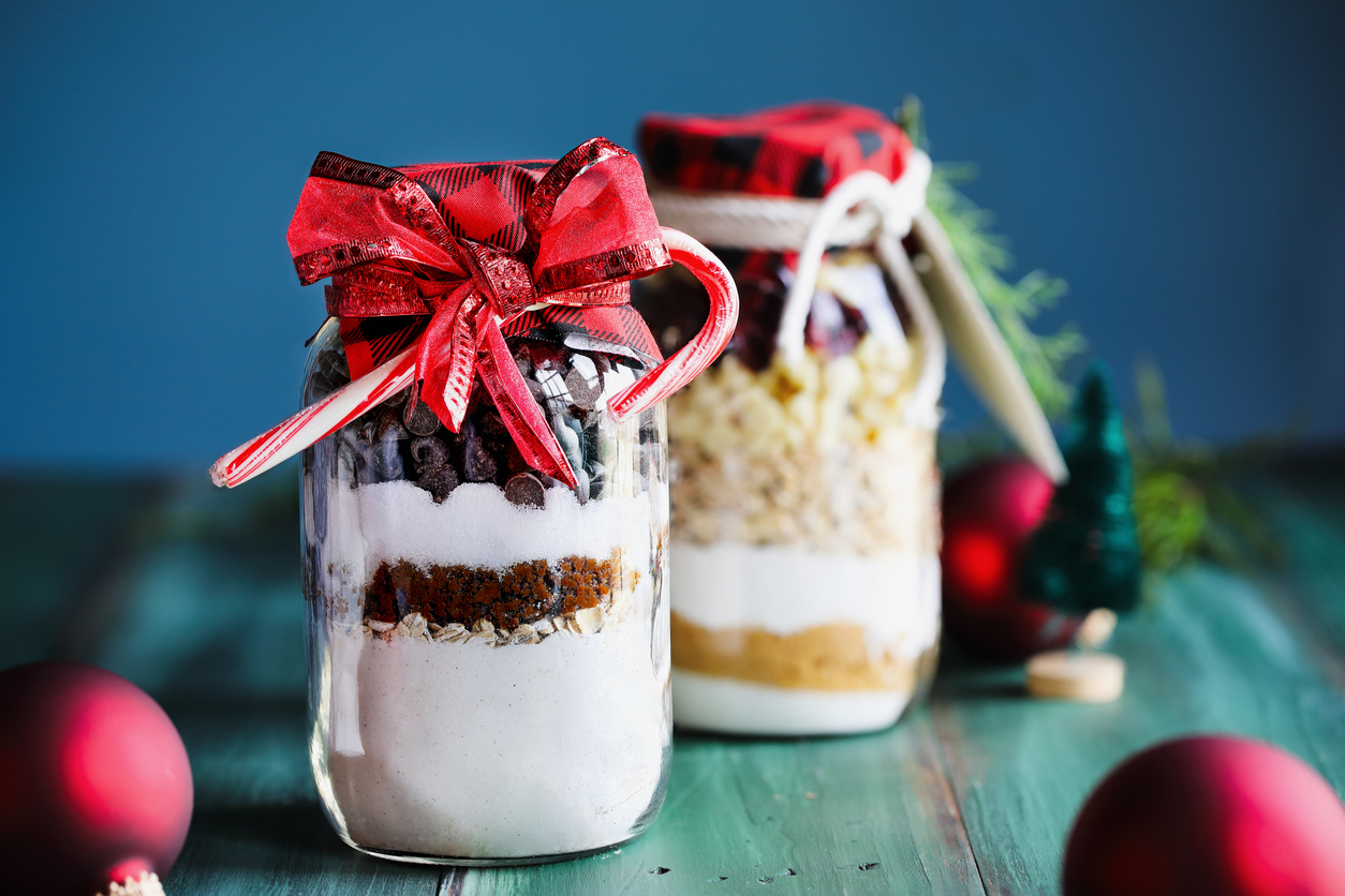 Variety of gifts of chocolate chip cookie dough and macadamia nut recipe mixture of ingredients for baking cookies for Christmas. Tied with a red ribbon and candy canes. Selective focus with blurred background.