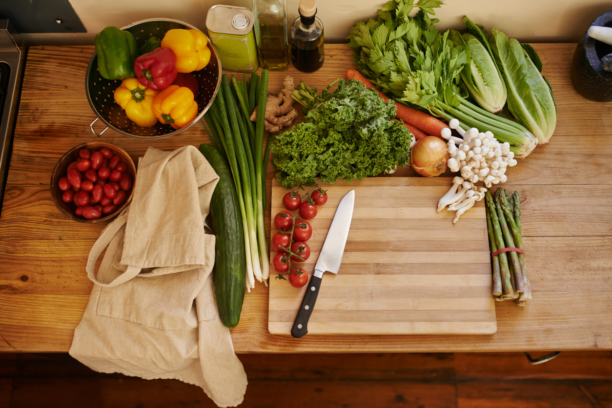 A variety of fresh vegetables rests on a freshly sealed butcher block in a kitchen. 