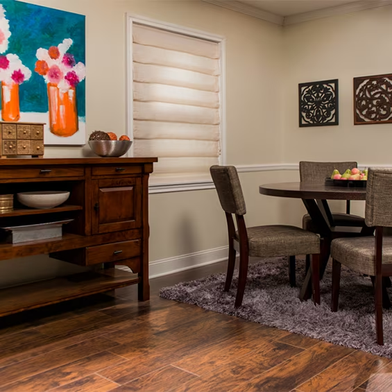 A small dining room with roman shades over a small window.