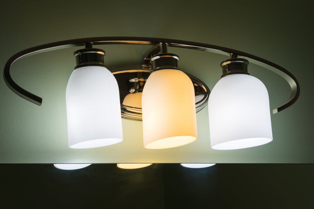 A bathroom vanity light fixture with two daylight bulbs and one soft white light bulb installed, all of which are turned on.