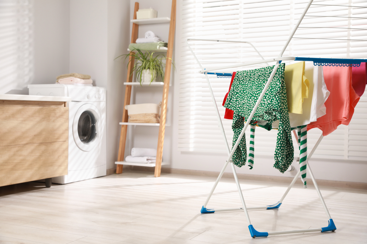 Colorful shirts on a foldable drying rack in a bright laundry room.