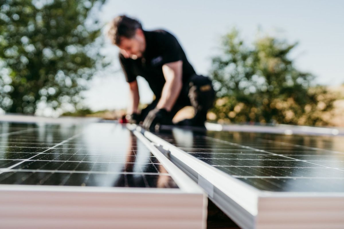 A worker dressed in black installs solar panels on a roof.