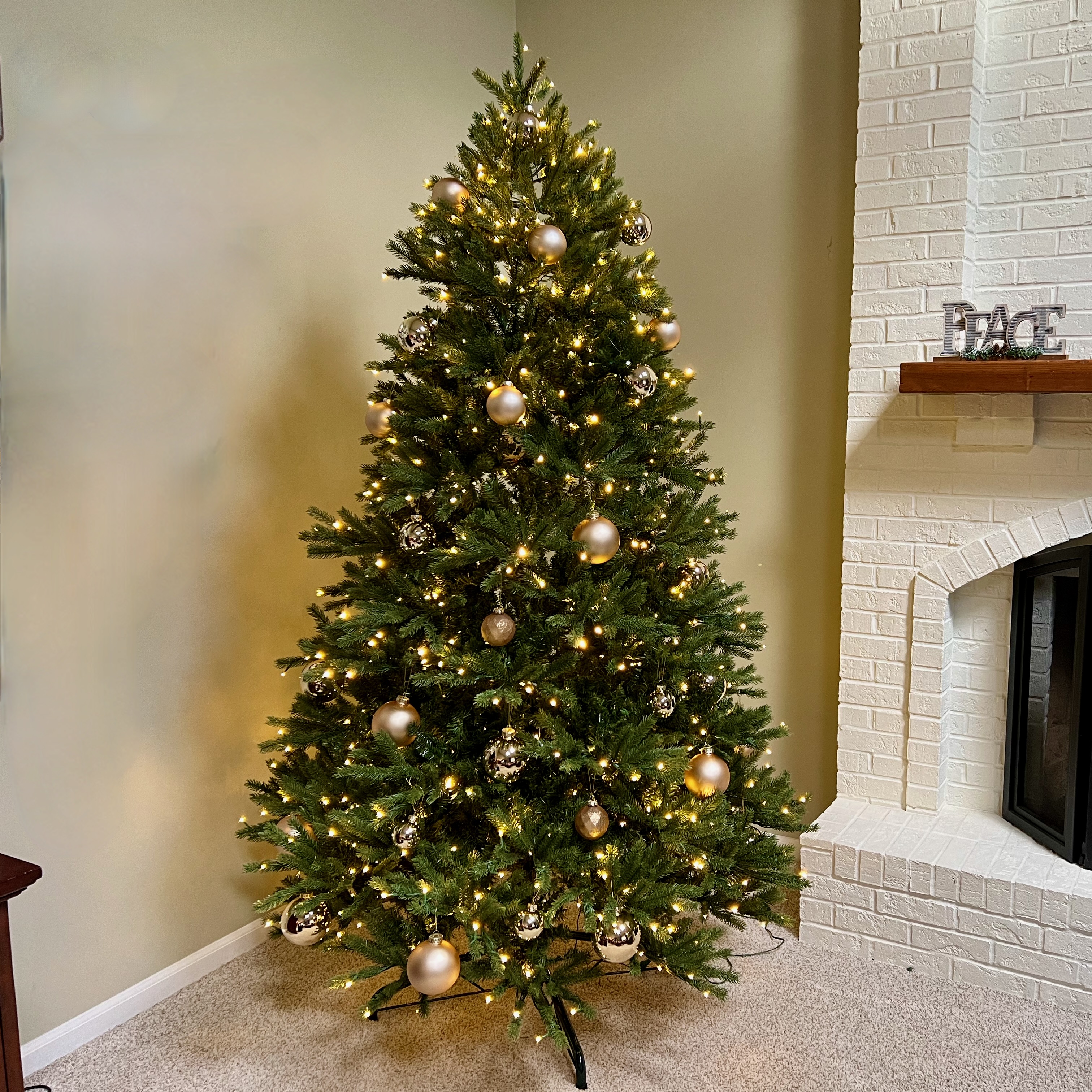 King of Christmas Fraser Fir artificial Christmas tree with gold ball ornaments in front of white fireplace