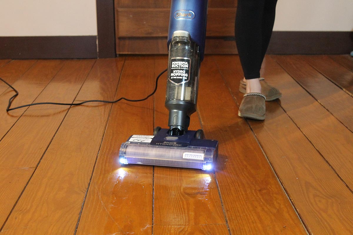 A person using the Shark HydroVac with LED lights to clean hardwood floors.