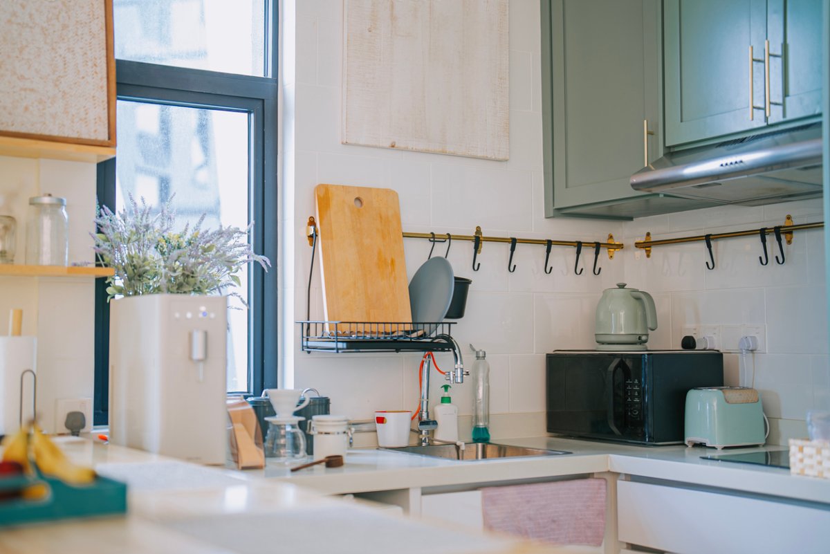 A small, cozy kitchen full of cute appliances with sage cabinets and slate-blue window trim.