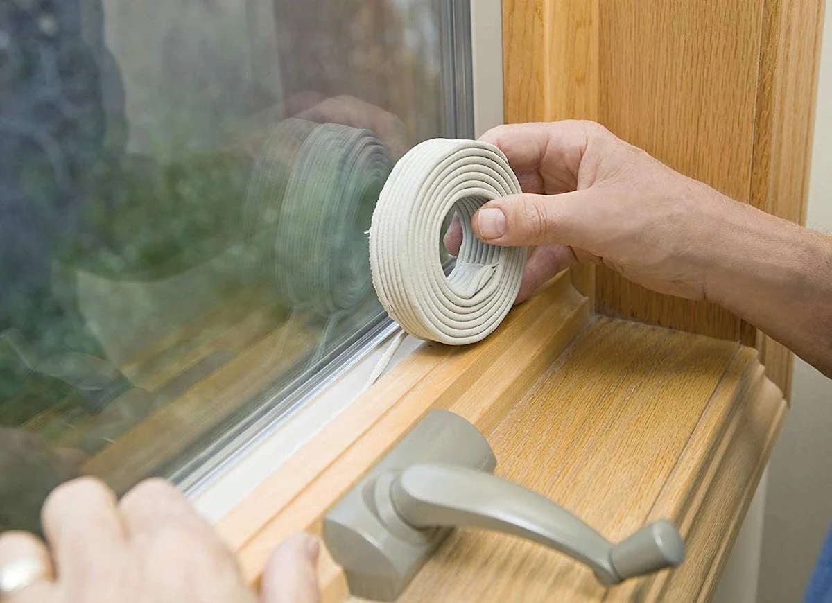 Hands using roll of caulking on window.