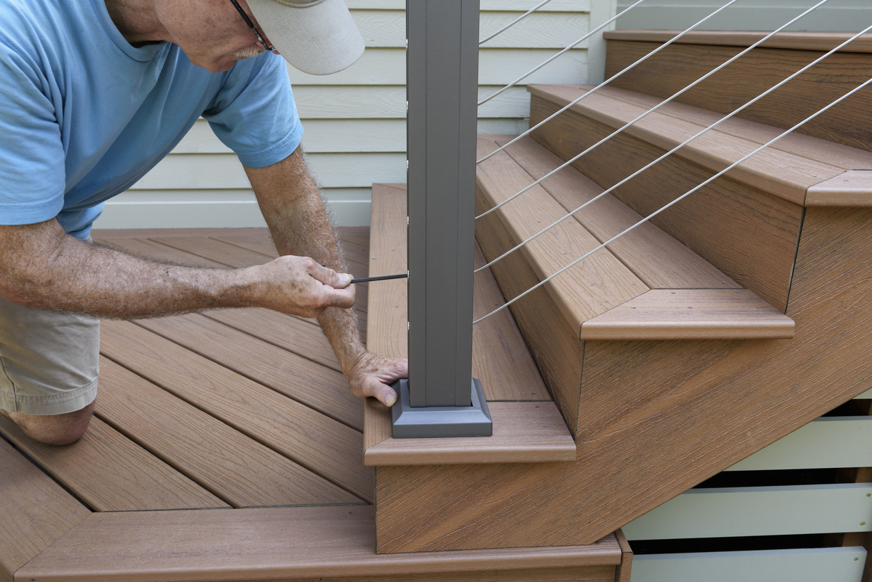 Worker using allen wrench to tighten wire railing on new composite wood deck with steps.