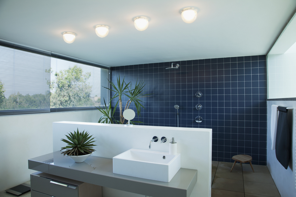 A-large-open-shower-is-tiled-with-navy-square-tiles-and-sits-behind-a-modern-white-and-grey-vanity.