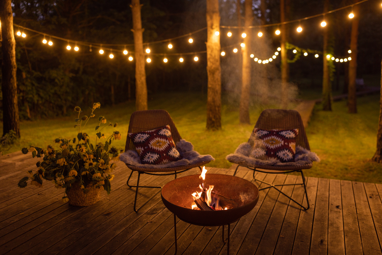 Comfortable arranged porch with fire pit and chairs. Autumn theme details. String lights in the background.