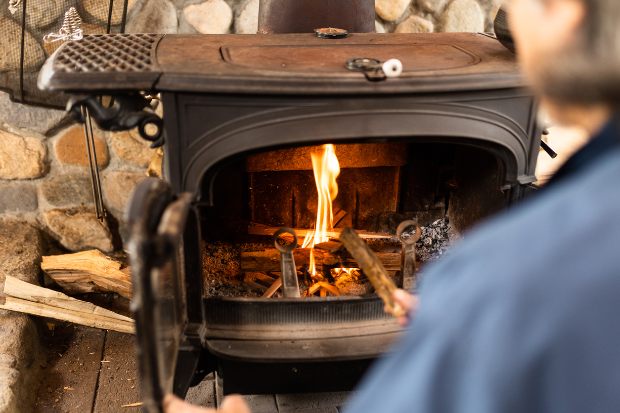 A-person-puts-wood-into-a-wood-burning-fireplace-that-is-lit.