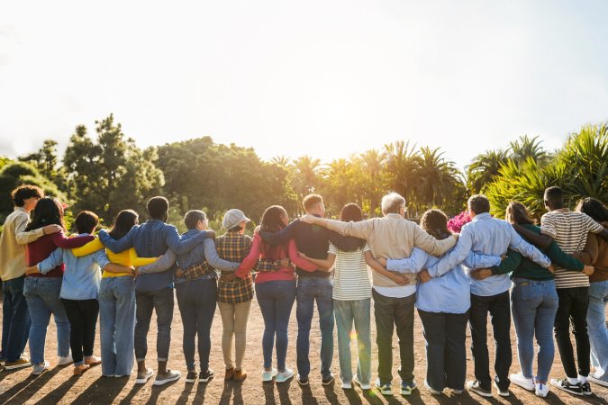 A-line-of-people-embrace-arm-in-arm-as-they-fact-away-toward-the-setting-sun-over-palm-trees.