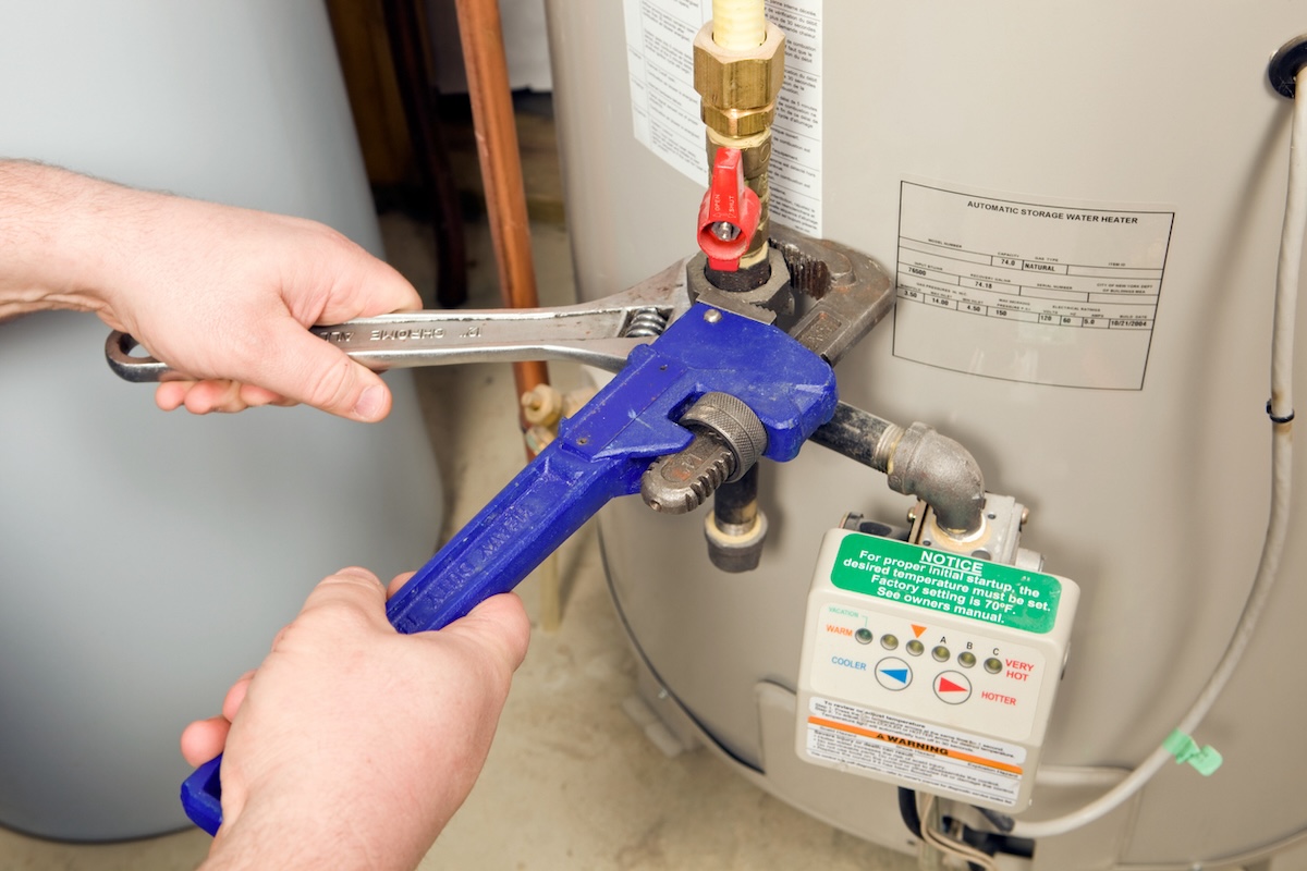 A plumber doing maintenance repairs on a home water heater expansion tank.