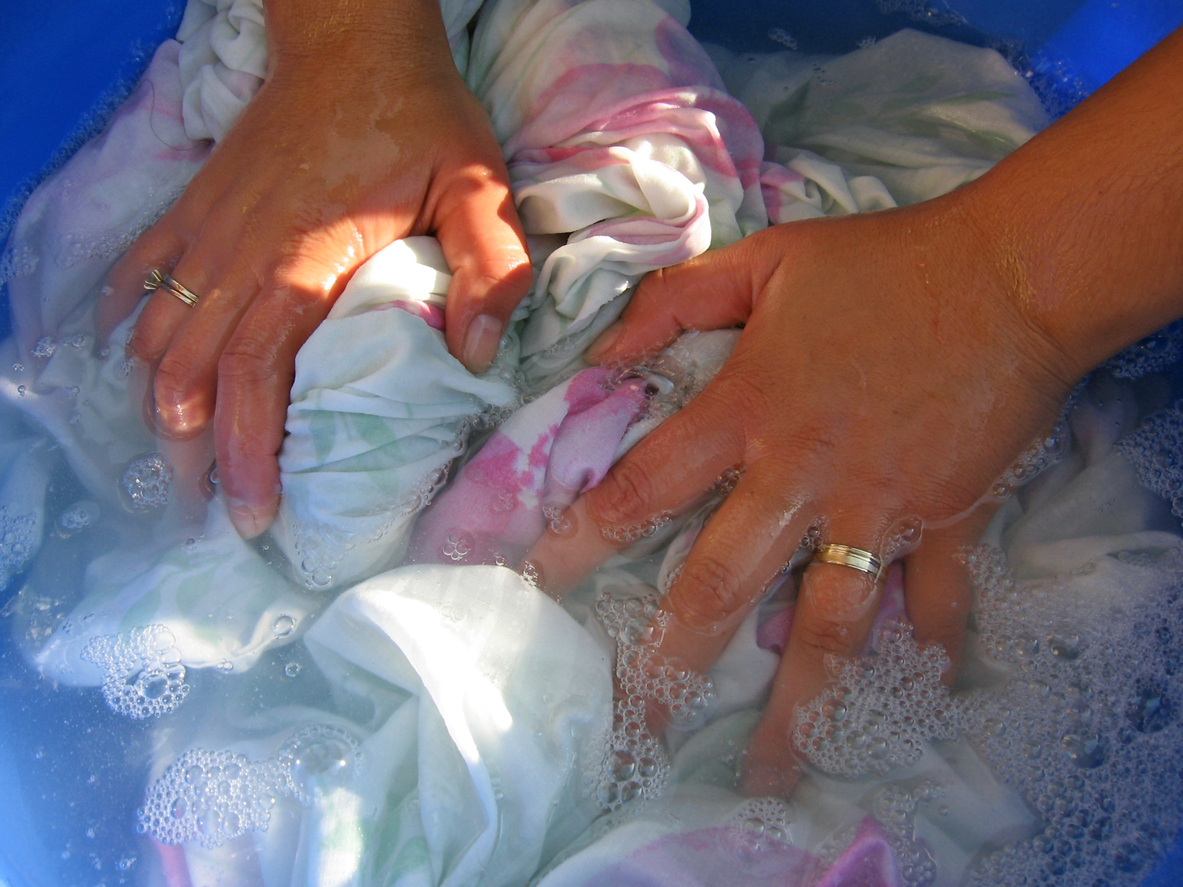 Woman uses hands to clean laundry soaking in water and soap.