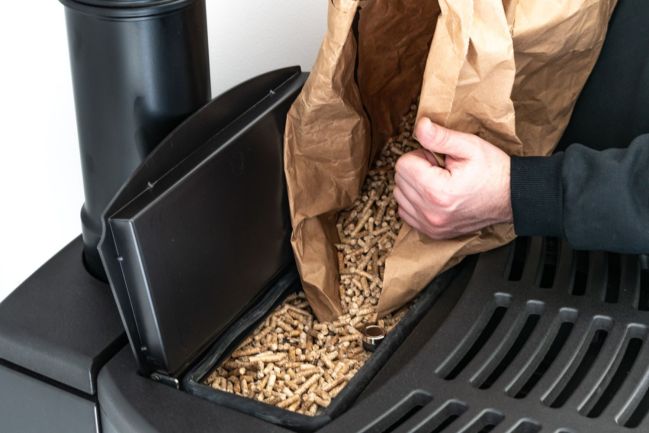 A close up of a person pouring pellets in a pellet stove. 