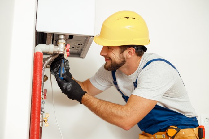 Side view of handyman, technician using screwdriver while fixing boiler or water heater, working on heating system in apartment. Manual work, maintenance,