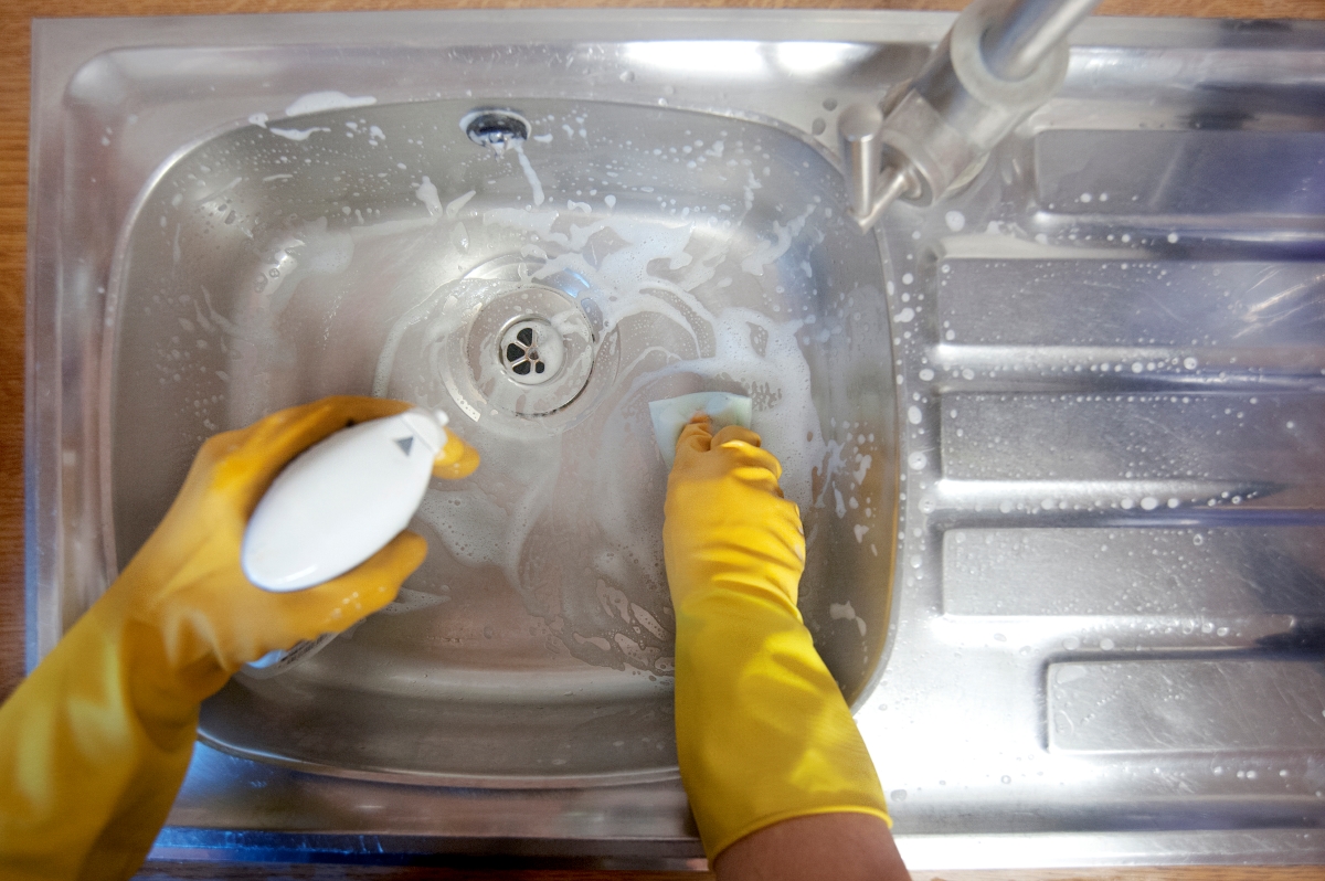 A person with yellow gloves is cleaning the kitchen sink with soap.