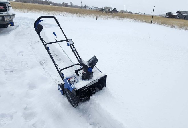 The Snow Joe Single-Stage Snow Blower on a large snow-covered cement pad during testing.