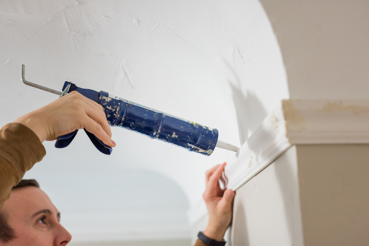 Man using a caulk gun to caulk crown molding.