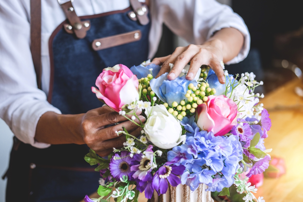 Person arranging faux flowers in vase.